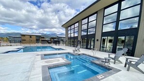 A pool area with multiple pools, lounge chairs, and a modern building with large windows.