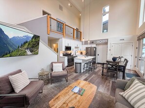 A spacious living area with a large island, a kitchen with white cabinets, and a view of a mountainous landscape.