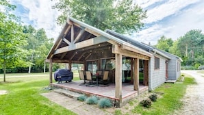 Ein modernes Haus mit überdachter Terrasse, Grill und gepflegtem Rasen.