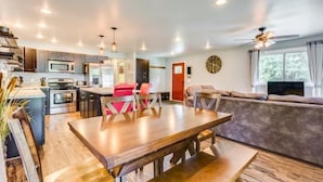 Eine moderne Küche mit eingebauten Geräten, ein Essbereich mit Holztisch und -stühlen sowie ein Wohnzimmer mit Sofa und Fernseher.