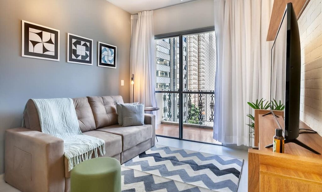 A modern living room with a sofa, a TV, and a balcony with curtains.