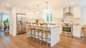 A modern kitchen with white cabinetry, a central island with bar stools, stainless steel appliances, and pendant lighting.