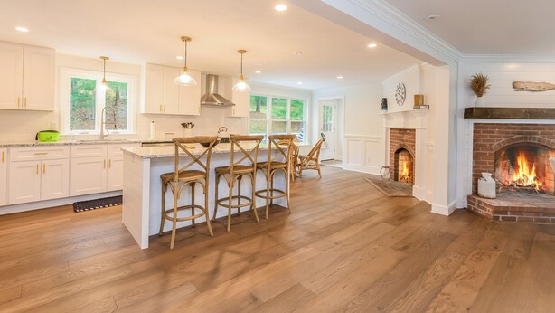 A spacious kitchen with wooden flooring, white cabinetry, and a central island with bar stools.