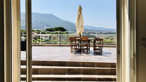 A view from a balcony with a table and chairs, a white umbrella, and a mountainous landscape in the background. - Beautiful apartment on 1st floor of a quiet villa in the countryside, near Ajaccio (Sarrola-Carcopino)