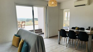 A modern living room with a sofa, a dining area with a table and chairs, and a large sliding glass door leading to a balcony. - Beautiful apartment on 1st floor of a quiet villa in the countryside, near Ajaccio (Sarrola-Carcopino)