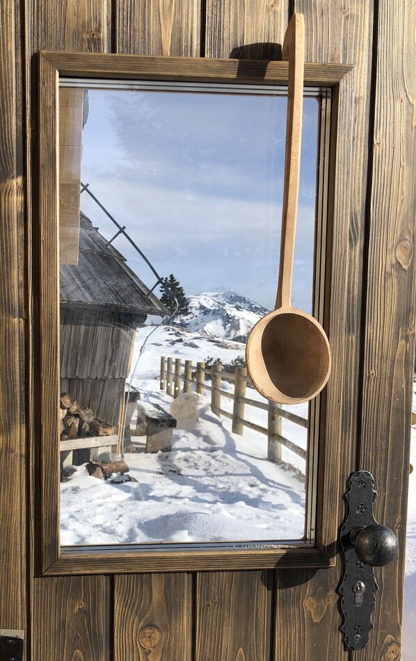 A wooden-framed window with a metal handle, reflecting a snowy mountain landscape.