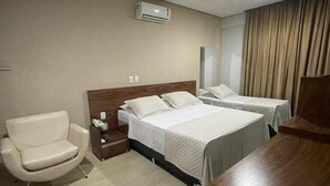 Ein Hotelzimmer mit zwei Betten, einem Sessel, einem Schreibtisch und einer Klimaanlage.
