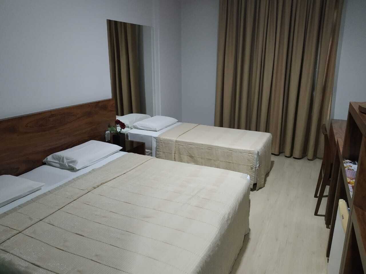 A hotel room with two beds, a wooden headboard, a small table with a bottle, and curtains.