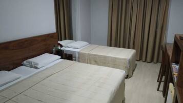 A hotel room with two beds, a wooden headboard, a small table with a bottle, and curtains.