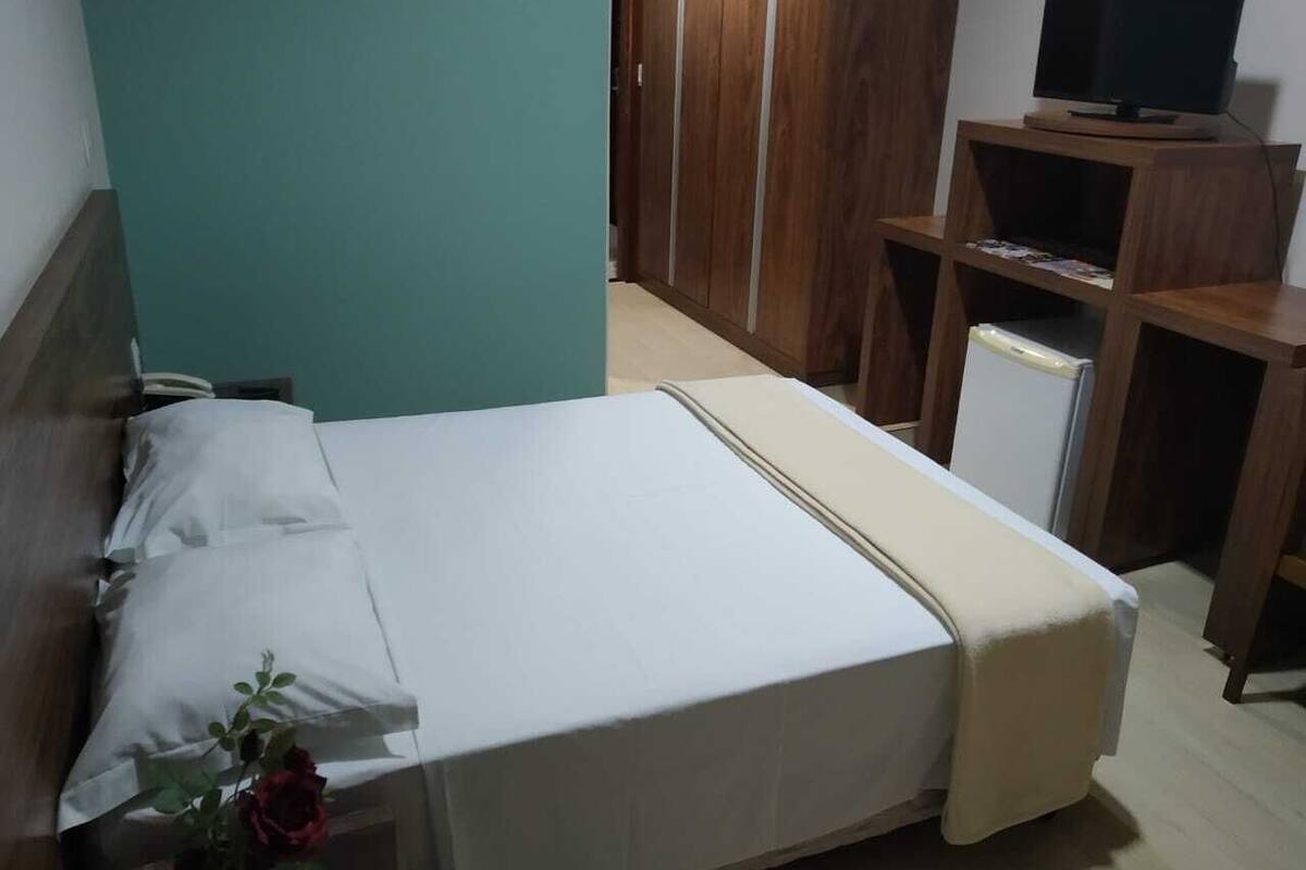 A neatly made bed with white linens, a wooden headboard, and a small bedside table with a vase of flowers.