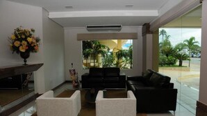 Eine Lobby mit einer schwarzen Couch, weißen Sessel, einem Couchtisch und einer Blumenvase.