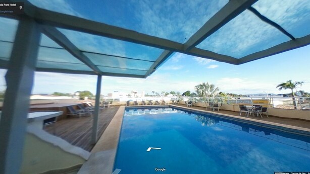 Ein Pool mit Glasdach, umgeben von Liegestühlen und Blick auf die Stadtlandschaft.