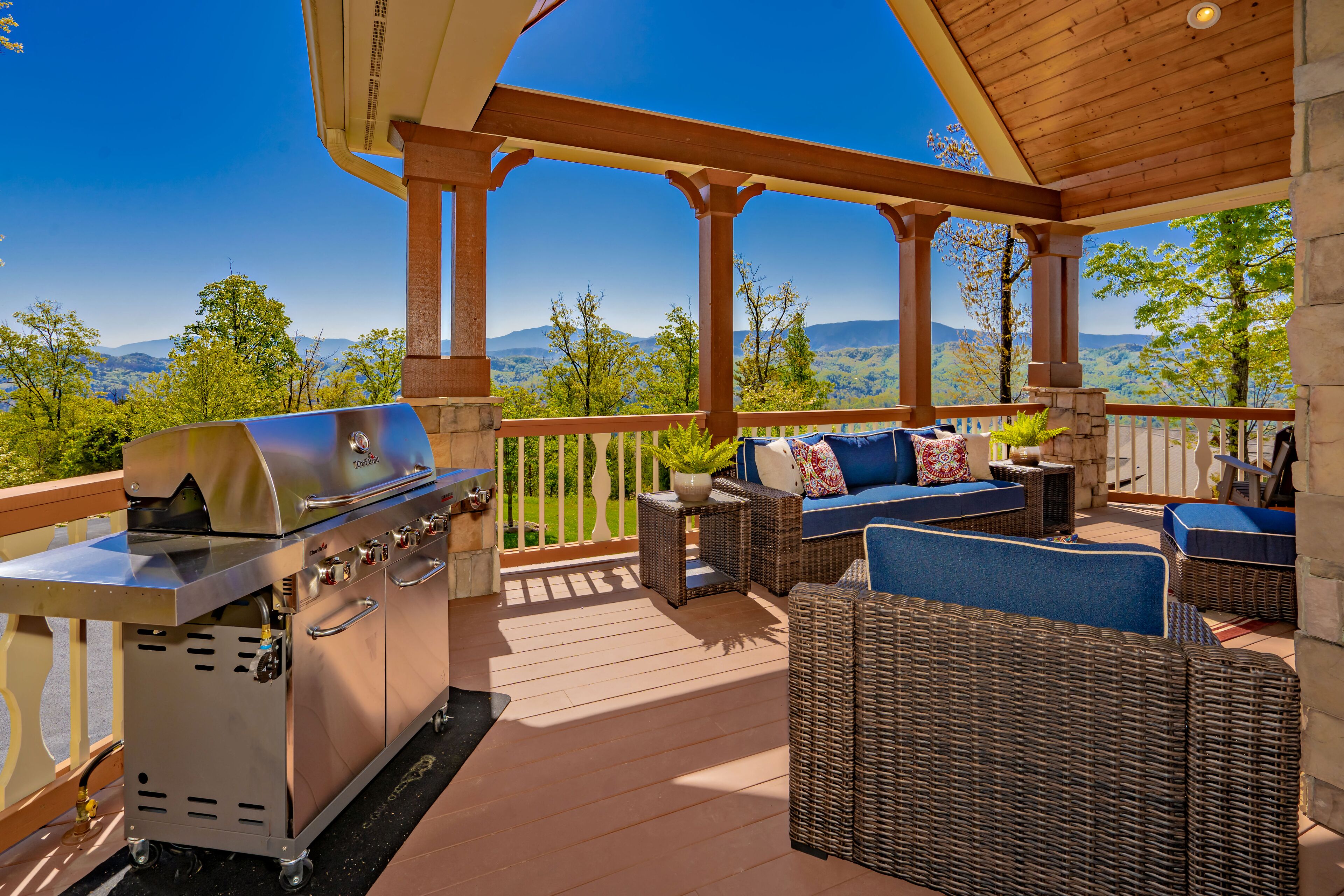 A covered outdoor deck with a grill, wicker furniture, and a scenic mountain view.