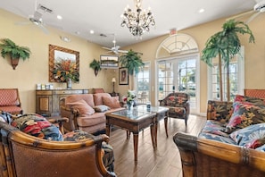 A spacious lobby with a high ceiling, ceiling fans, a chandelier, and large windows allowing natural light.