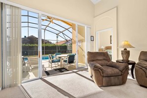 A living room with a sliding glass door leading to a patio with a pool, a brown armchair, a lamp, and a small table. - 64 - Great 4 bedroom villa with south facing pool (Davenport)
