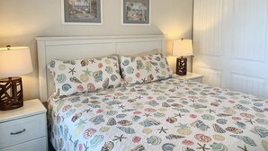 A bedroom with a bed, two bedside tables, a nightstand, a ceiling fan, and two wall-mounted lamps. - Oceanfront, Pet-Friendly Condo with Private Balcony! (St. Augustine)