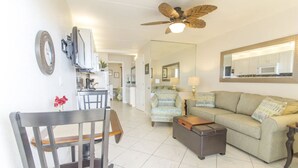 A living room with a sofa, a coffee table, a chair, a ceiling fan, and a kitchen area in the background. - Oceanfront, Pet-Friendly Condo with Private Balcony! (St. Augustine)