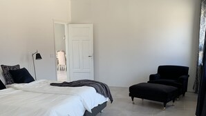 Un dormitorio moderno con una cama grande, un sillón negro y un pequeño reposapiés.
