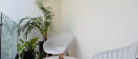 Un balcón pequeño y cerrado con una silla blanca, una mesita y plantas en macetas.