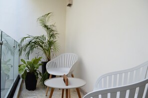 Un petit balcon fermé, avec une chaise blanche, une petite table et des plantes en pot.