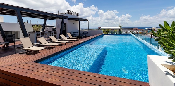 Une piscine sur le toit, dotée de chaises longues et offrant une vue sur l’océan.