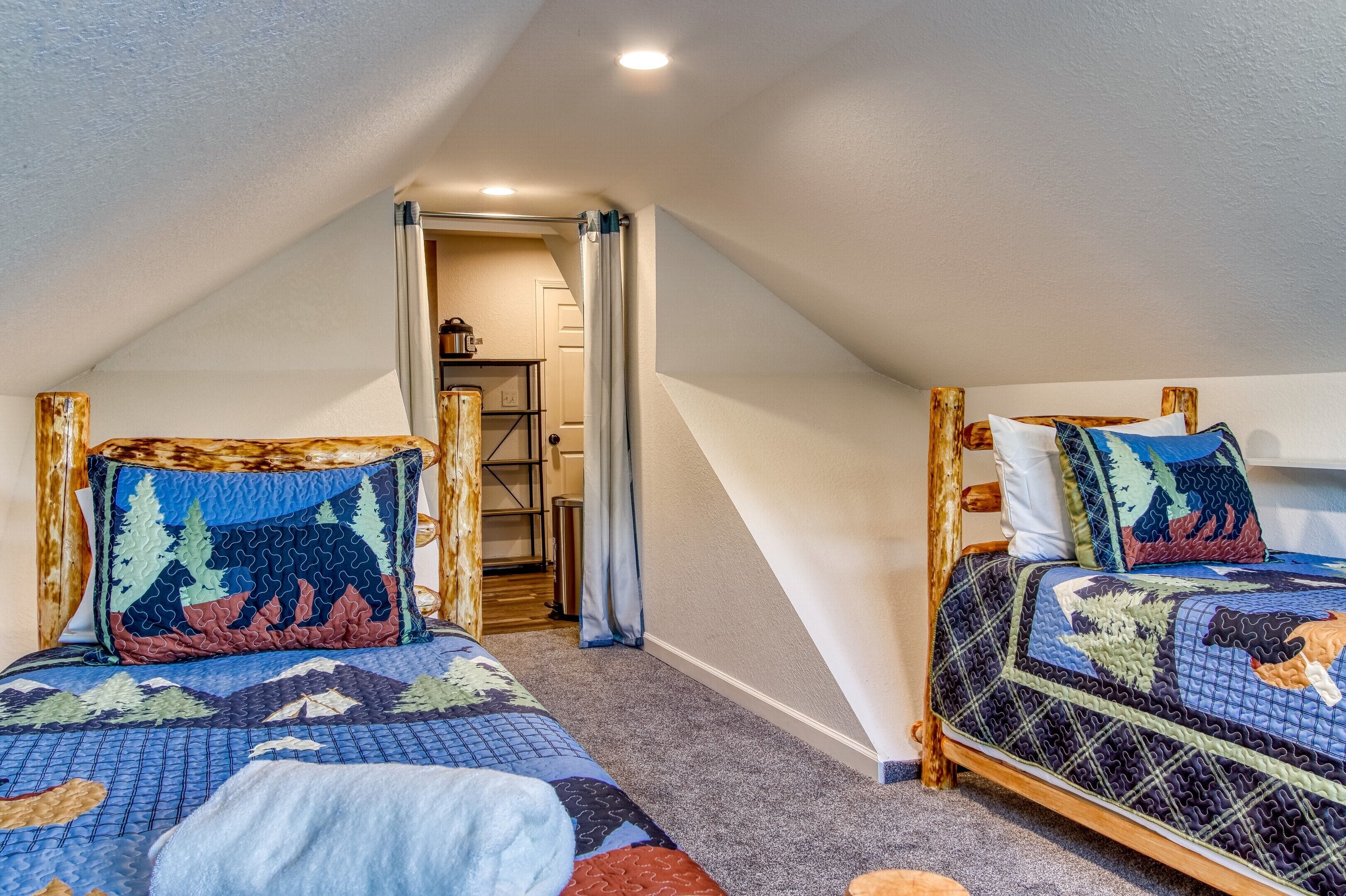 Two single beds in a room with a sloped ceiling, wooden headboards, and a quilted bedspread.