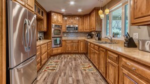 A kitchen with wooden cabinets, stainless steel appliances, and a large window. - Rustic River Lodge by HoneyBearCabins (Sevierville)