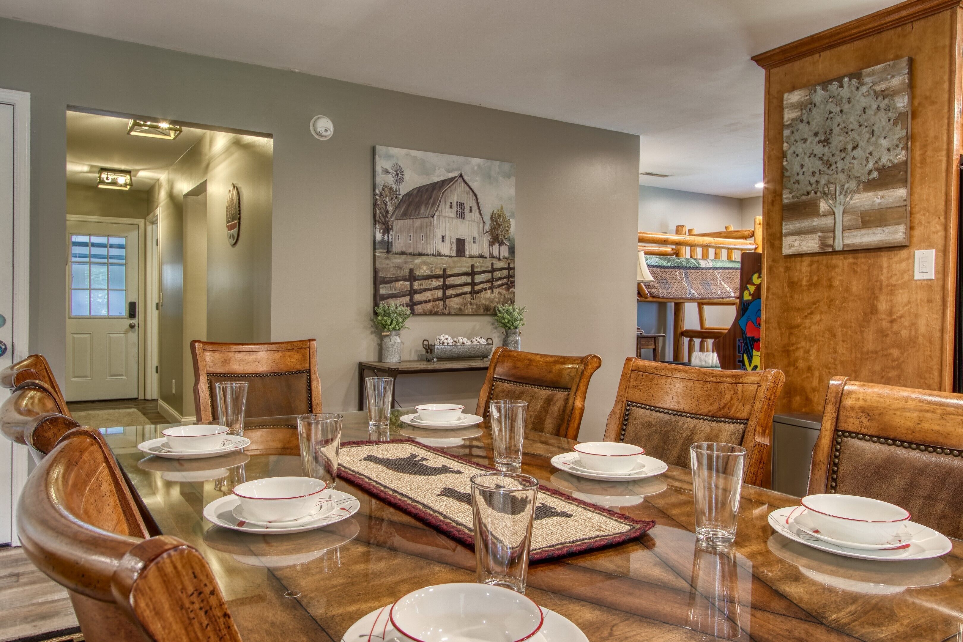 A dining area with a wooden table set for six, surrounded by wooden chairs.