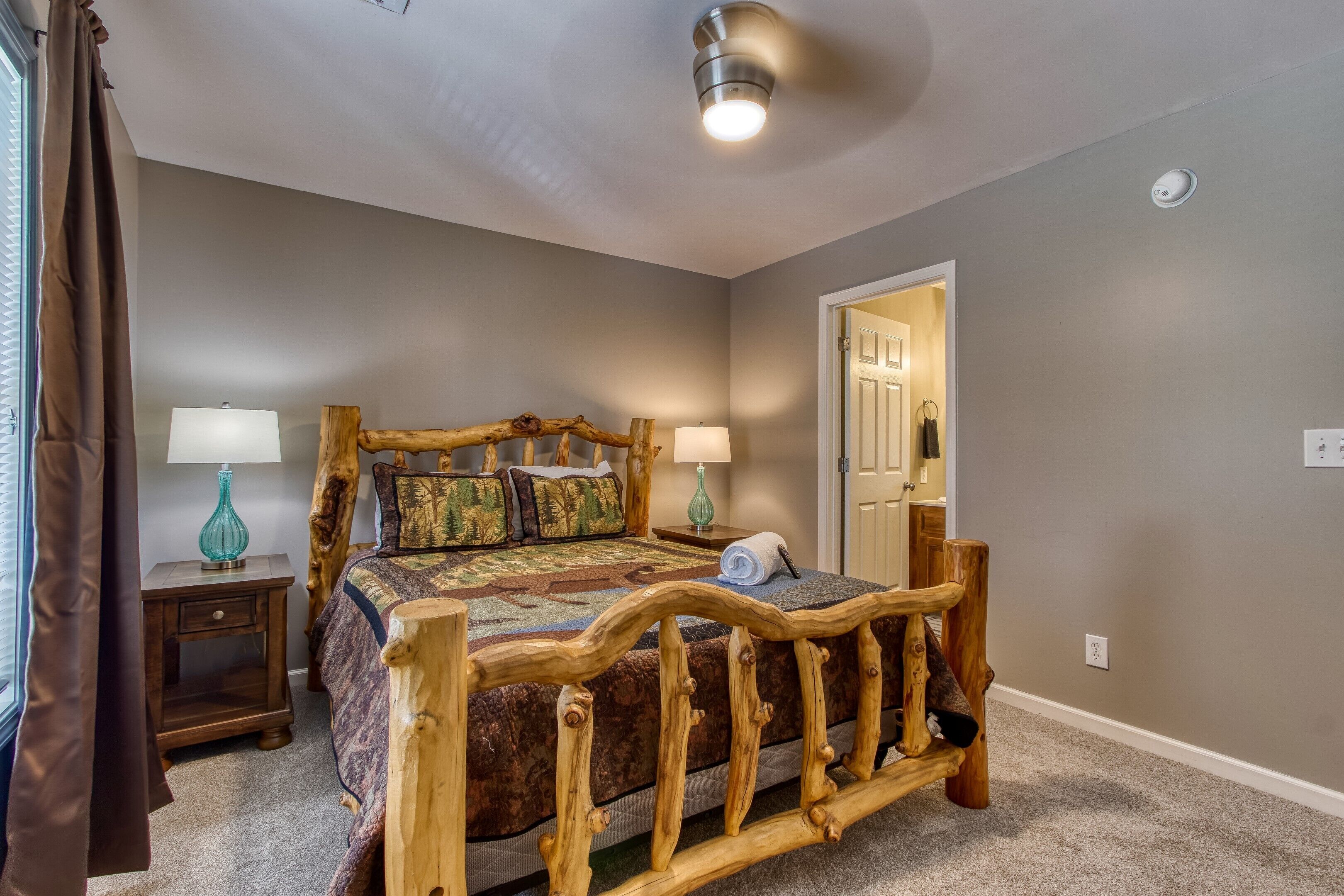 A bedroom with a wooden bed, two bedside tables, a lamp, and a door leading to another room.