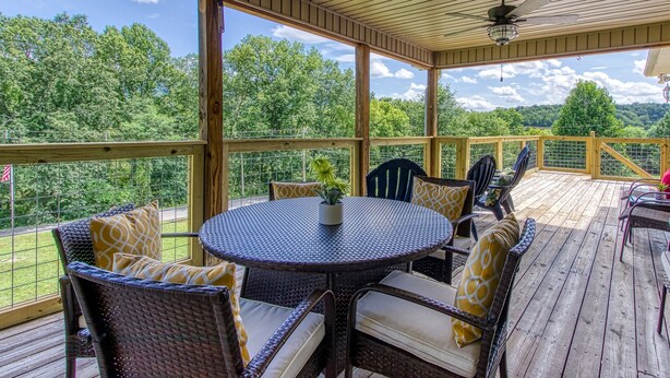 A covered outdoor deck with wicker furniture, a round table, and a ceiling fan. - Rustic River Lodge by HoneyBearCabins (Sevierville)