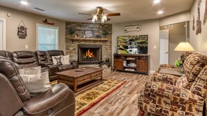 A living room with leather sofas, a fireplace, a television, and a ceiling fan. - Rustic River Lodge by HoneyBearCabins (Sevierville)