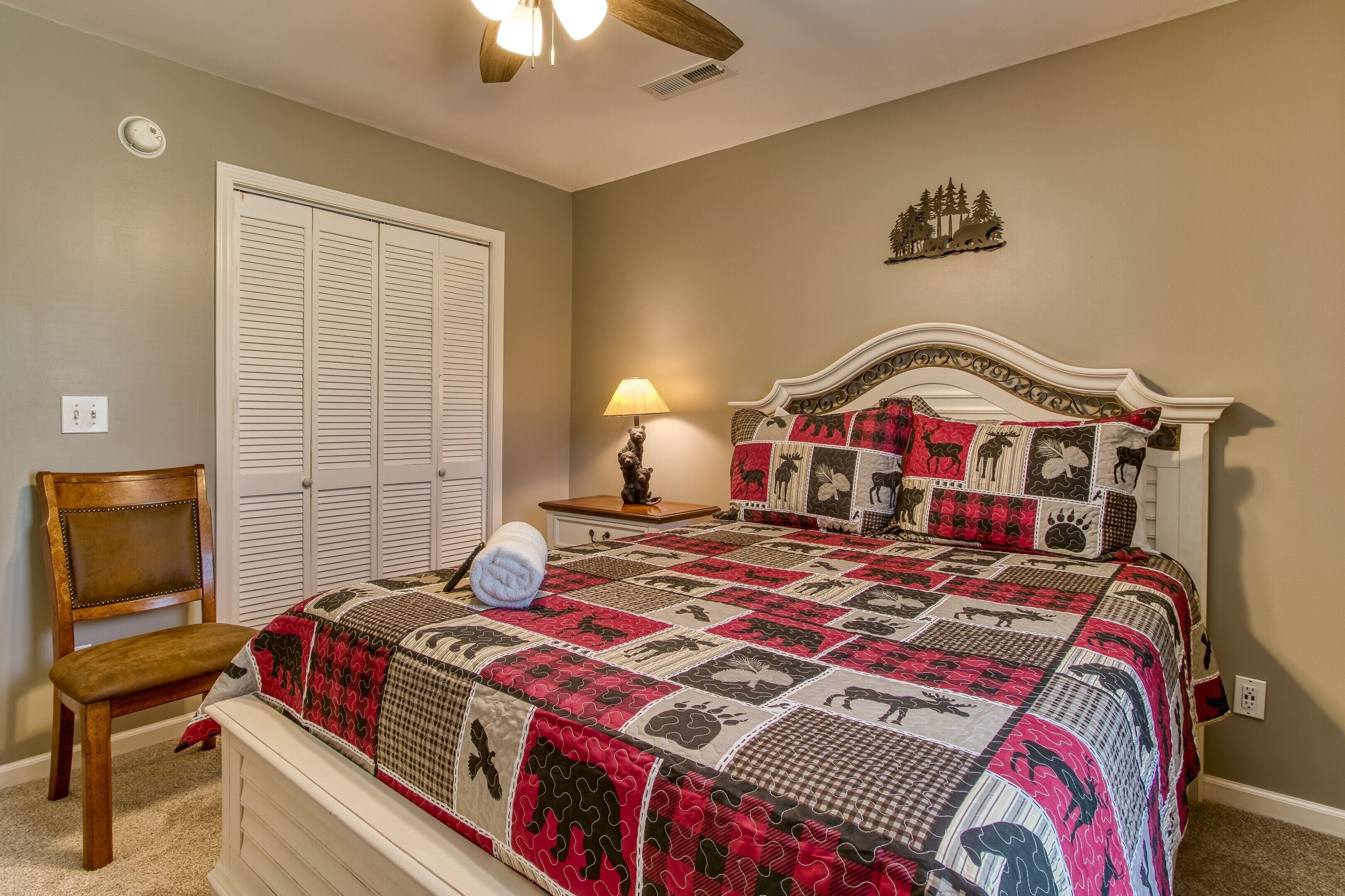 A bedroom with a large bed, a chair, a nightstand with a lamp, and a closet.