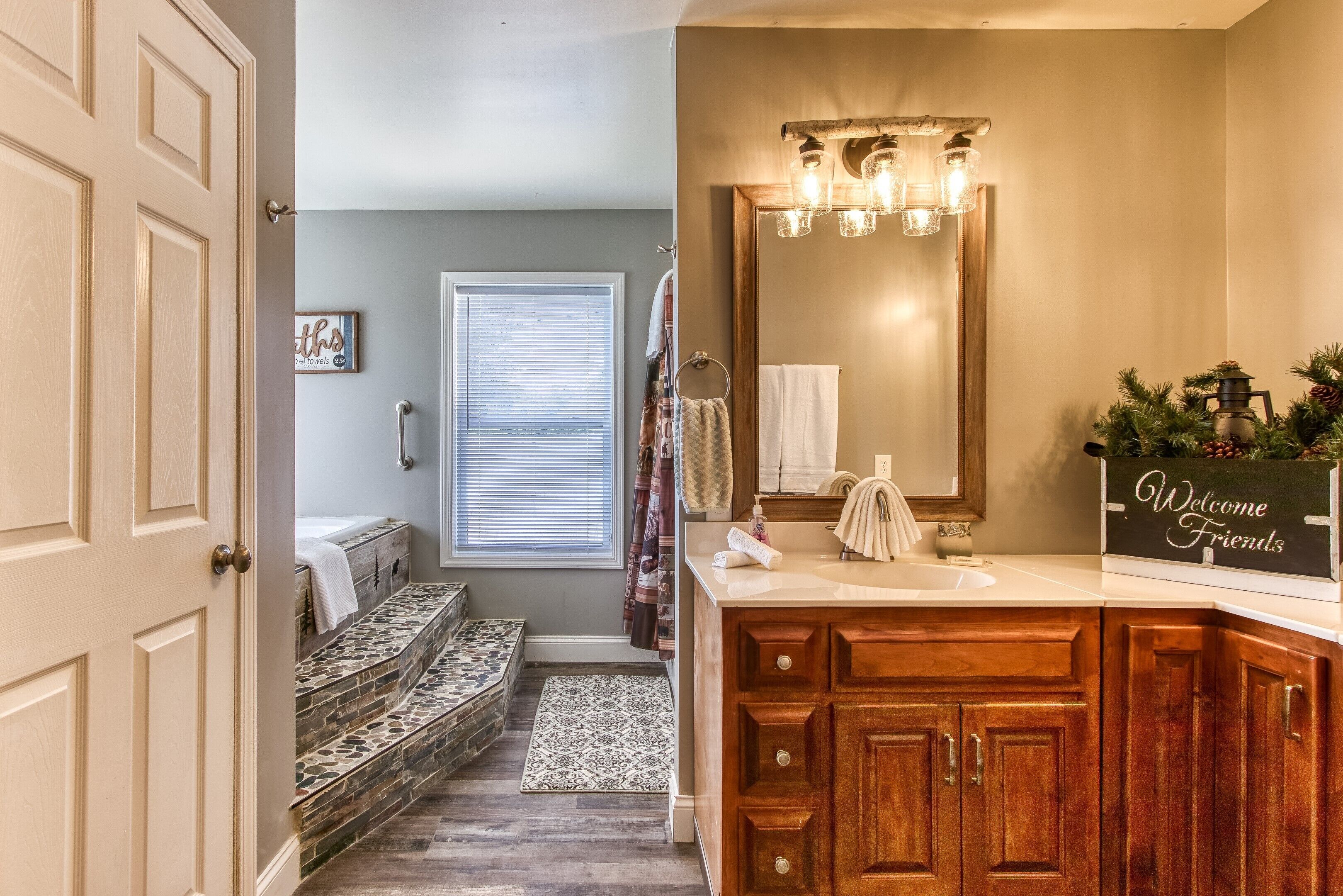Une salle de bain avec un meuble-lavabo en bois, un grand miroir et une pancarte sur laquelle on peut lire « Bienvenue, amis ».