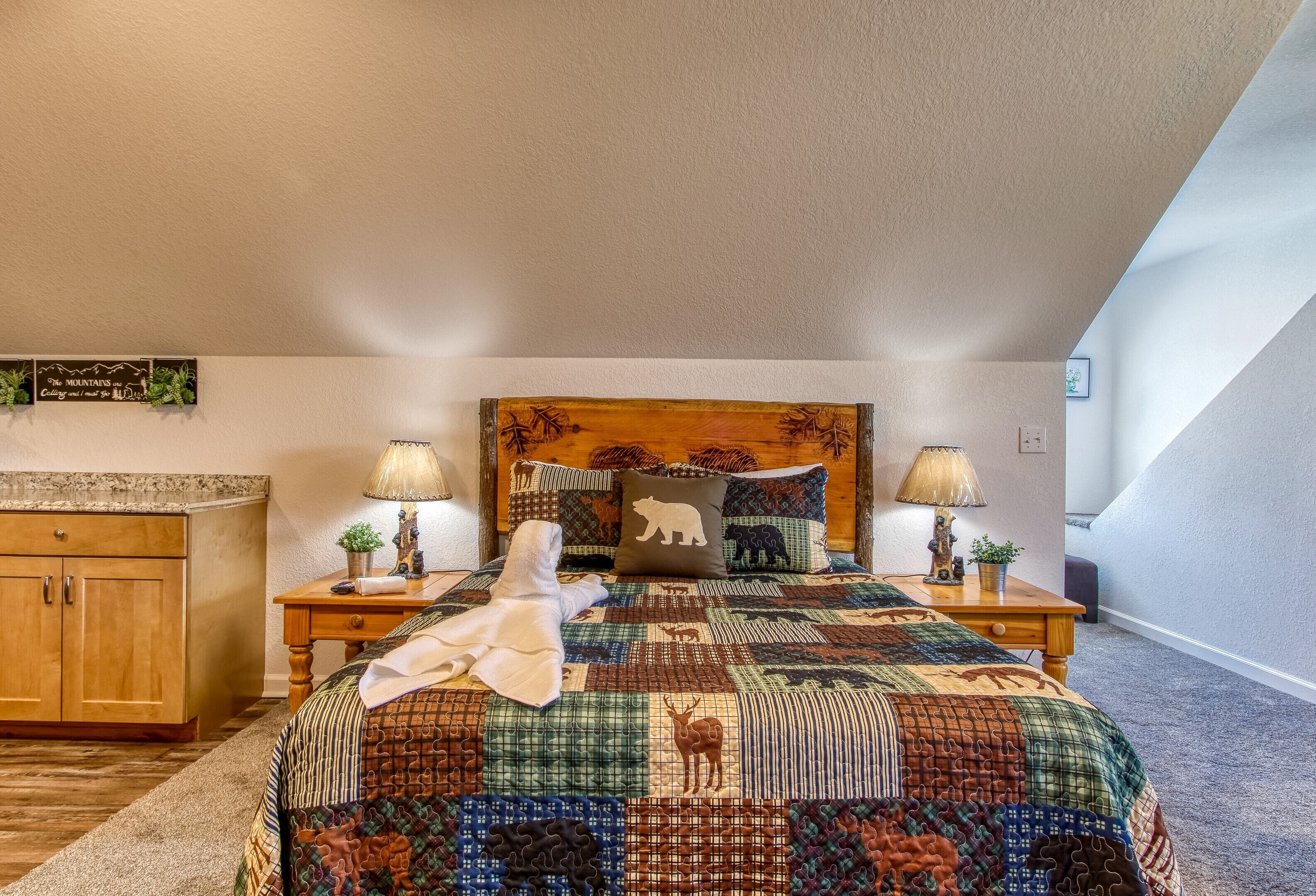 Een slaapkamer met een groot bed, twee nachtkastjes, een houten hoofdbord, een sprei en een klein bureau met een lamp.