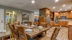 A spacious kitchen with wooden cabinets, a dining table set for six, and modern appliances. - Rustic River Lodge by HoneyBearCabins (Sevierville)