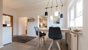 A modern kitchen with wooden cabinets, a dining table with chairs, and pendant lights.