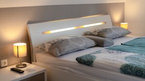 A neatly made bed with patterned pillows and a quilt, a bedside lamp, and a remote control on a nightstand.