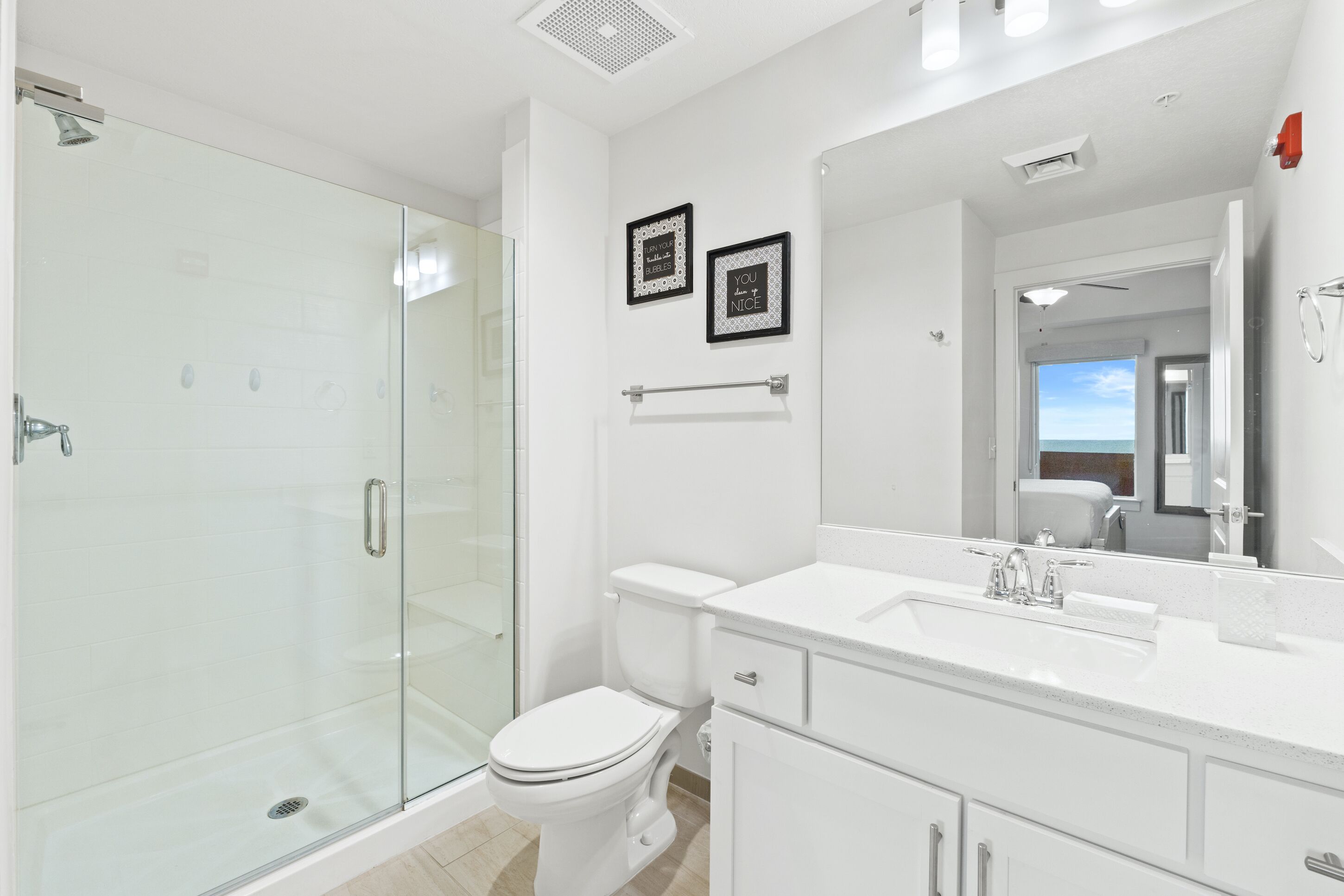 A modern bathroom with a glass shower enclosure, a white toilet, and a large mirror above the sink.