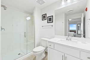 A modern bathroom with a glass shower enclosure, a white toilet, and a large mirror above the sink.