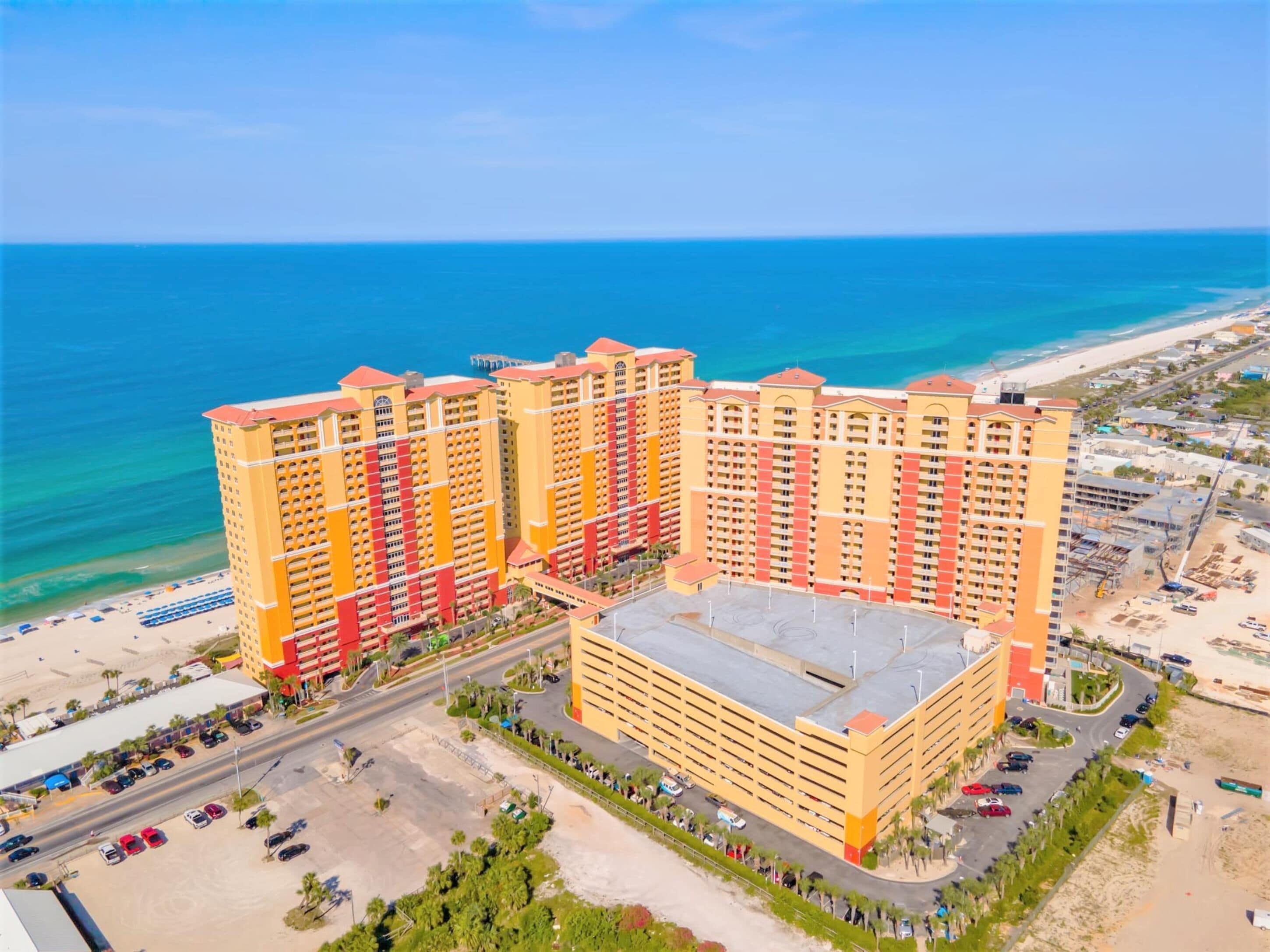 Un hôtel à plusieurs étages doté d’une cour intérieure, situé près d’une plage aux eaux d’un bleu cristallin.