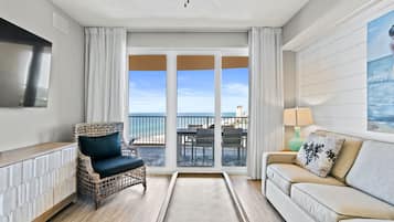 A room with a view of the beach, a wicker chair, a sofa, a TV, and a lamp.