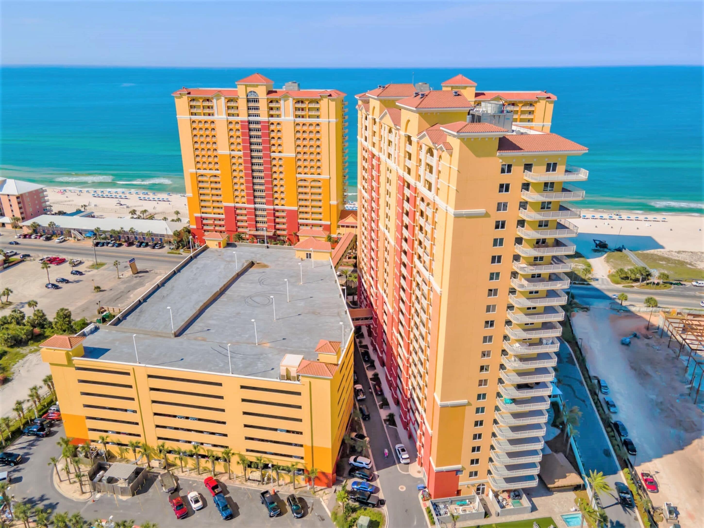 A multi-story hotel with a parking lot and a beach view.