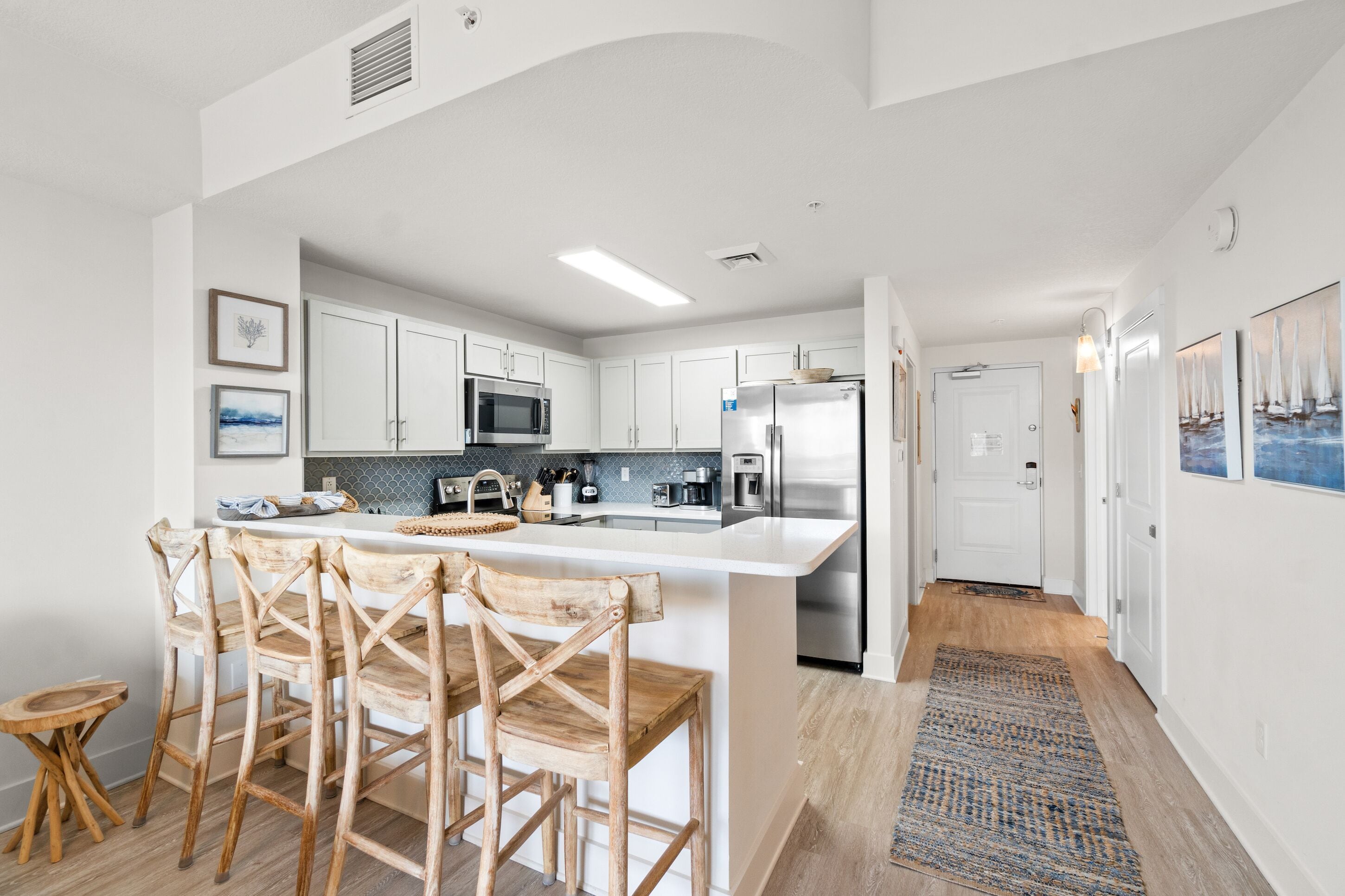 Una cocina moderna con armarios blancos, una isla central, sillas de madera y una pequeña mesa de comedor.