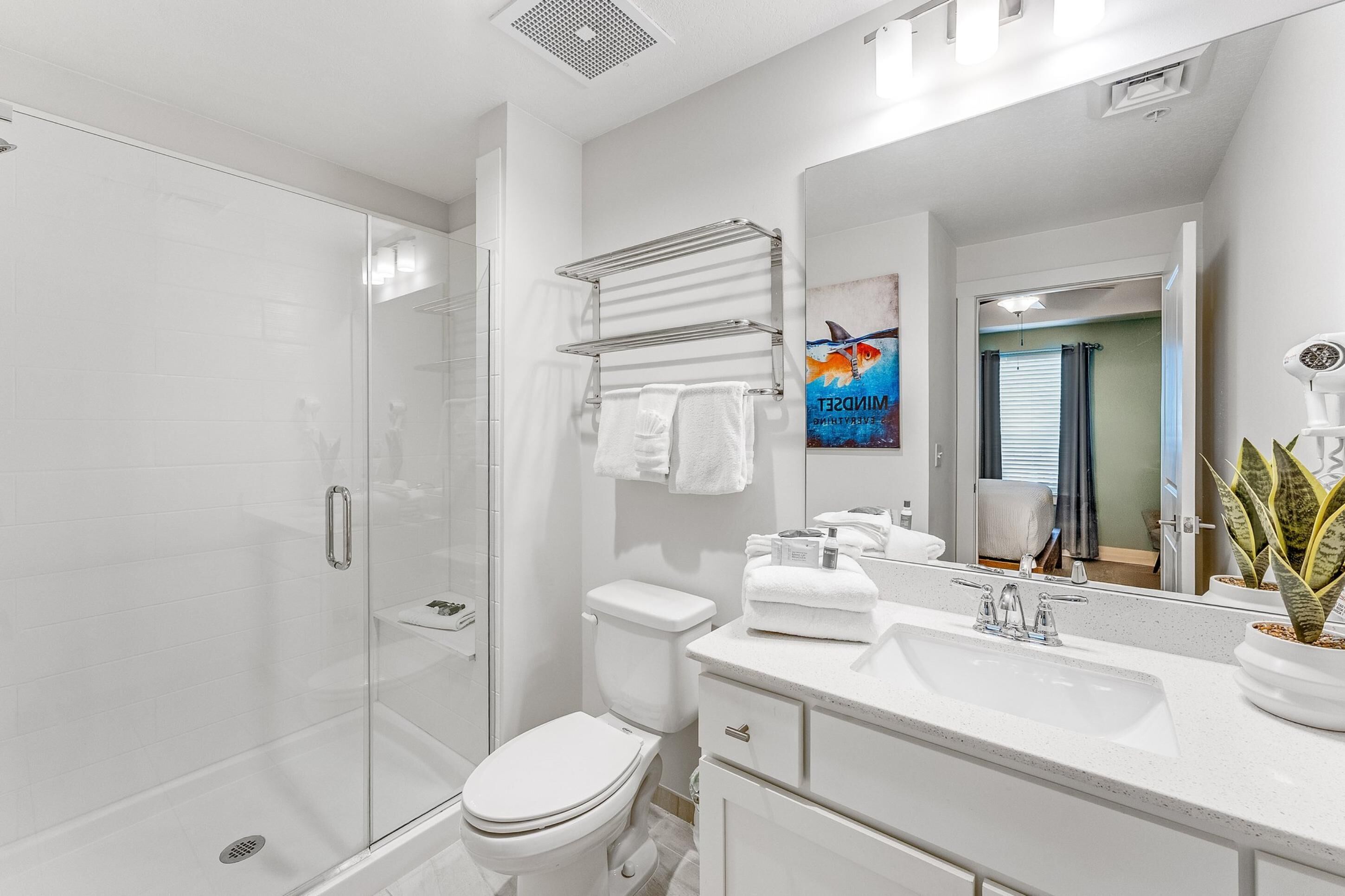 Une salle de bain moderne avec une douche à parois de verre, des toilettes blanches, un lavabo avec un miroir et un porte-serviettes.