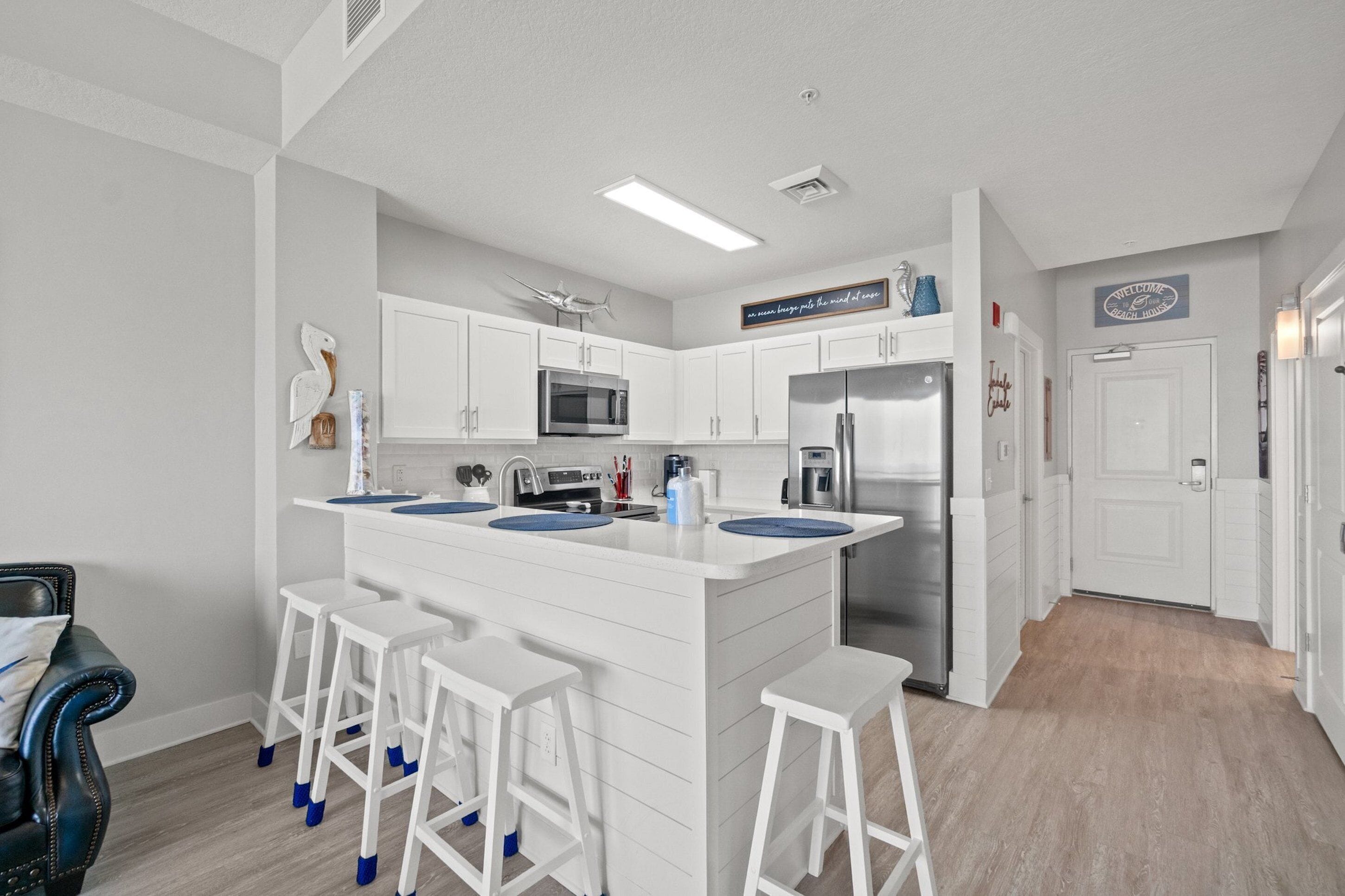 A modern kitchen with white cabinetry, a central island with stools, stainless steel appliances, and a "Welcome" sign.