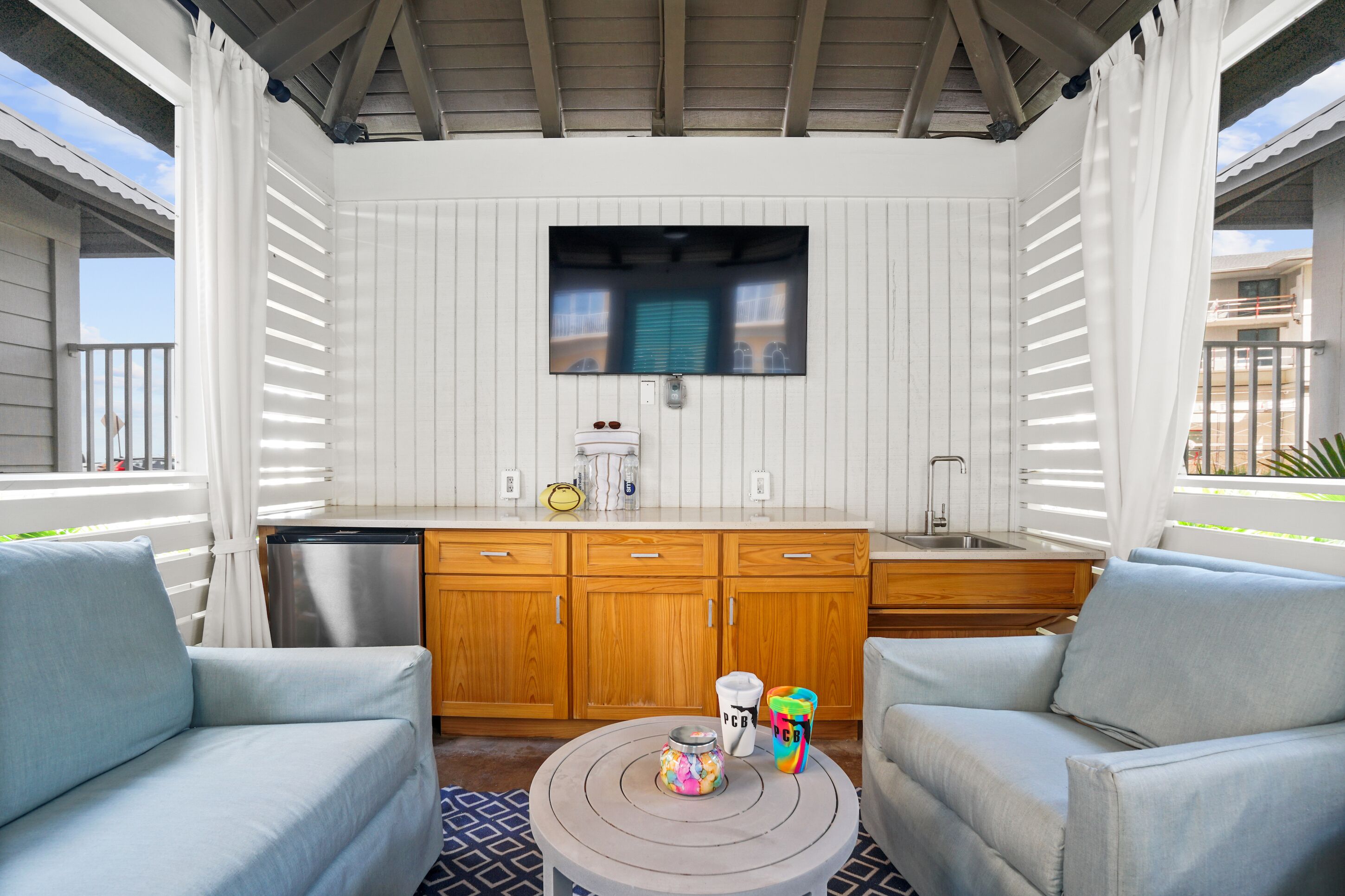 A covered outdoor area with a wooden cabinet, a sink, and two light blue sofas.