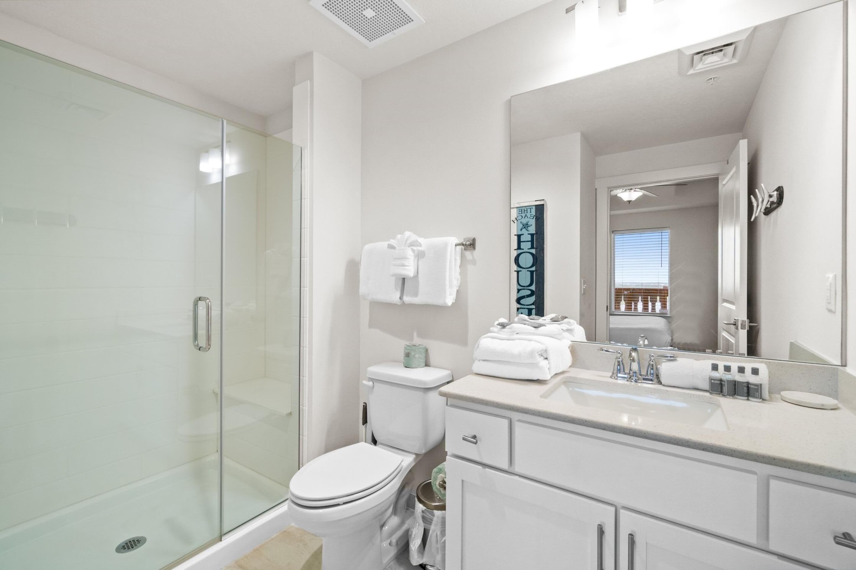 A modern bathroom with a glass shower enclosure, a white toilet, a vanity with a sink and mirror, and a towel rack with folded towels.