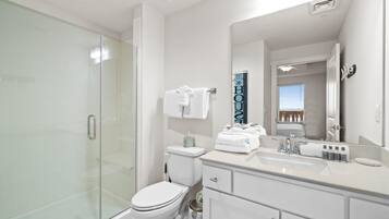 A modern bathroom with a glass shower enclosure, a white toilet, a vanity with a sink and mirror, and a towel rack with folded towels.