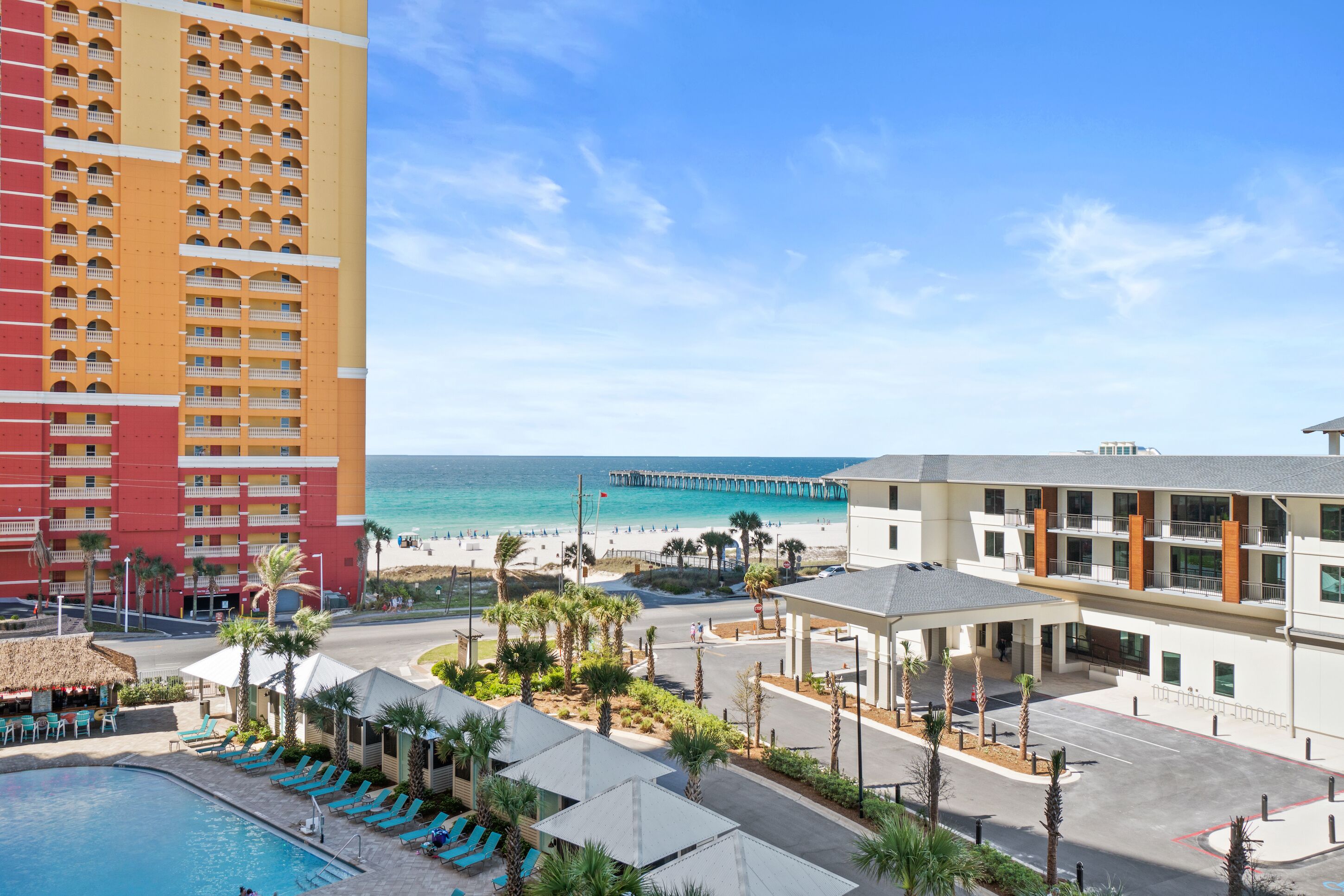 A hotel with a pool, beach view, and a pier in the background.