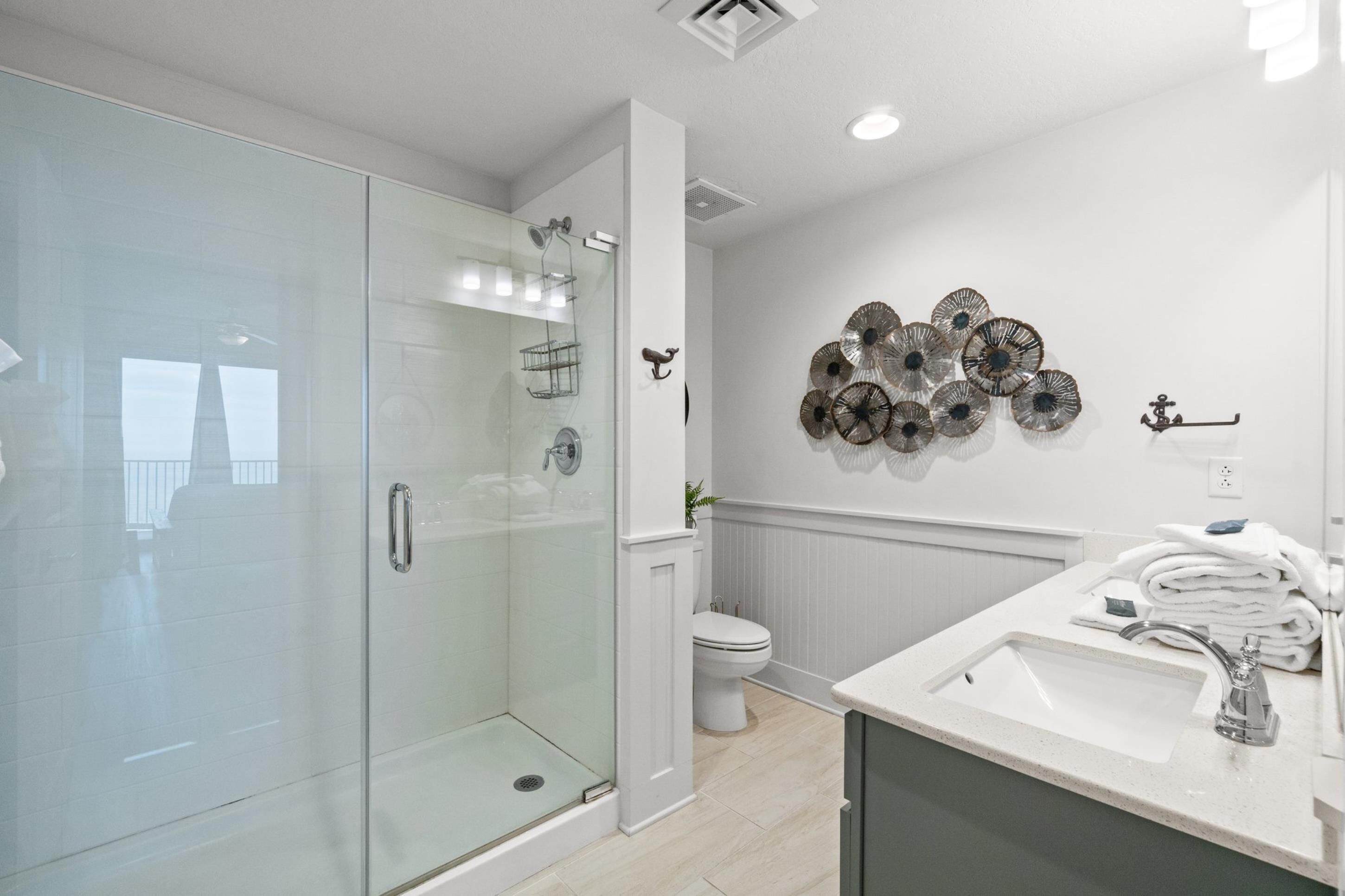 Un baño moderno con cabina de ducha de vidrio, inodoro y lavamanos con una pila de toallas.